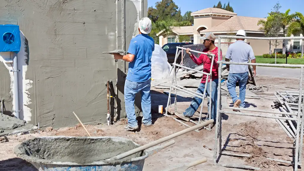 Three-man crew applying fresh cement stucco to exterior wall with trowels and scaffolding – Toms River Stucco