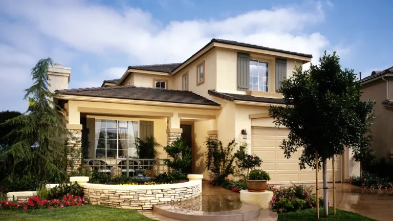 Two-story beige stucco home with stone accent walls, dark roof tiles and landscaped front yard – Toms River Stucco