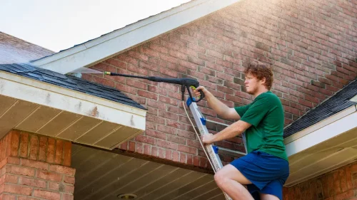 Man on ladder pressure washing brick exterior and gutters of a residential home – Toms River Stucco